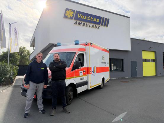 Zwei Männer stehen vor einem Rettungswagen vor dem Firmengebäude der Veritas Ambulanz